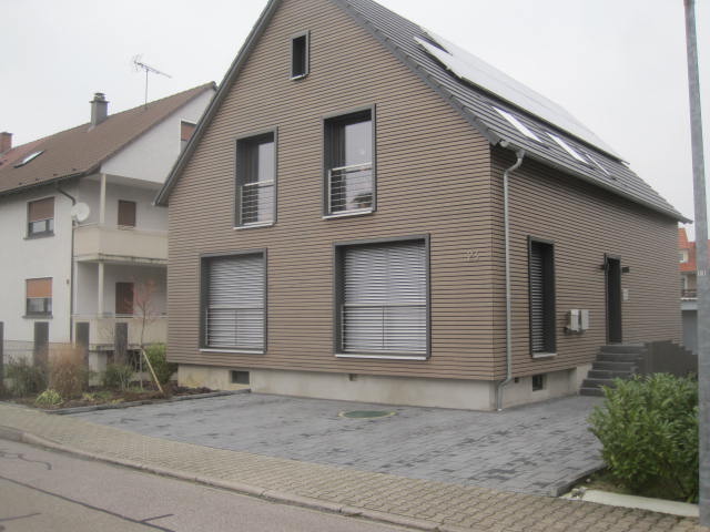 Ein modernes zweistöckiges Haus mit braunem Fassadenverkleidung, geschlossenen Jalousien und einem gepflasterten Vorgarten.